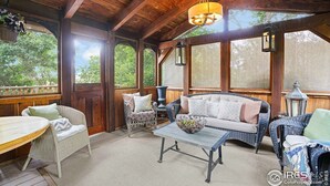 Un porche cubierto con vigas de madera, muebles de mimbre y una lámpara colgante.