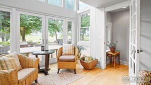 Un luminoso espacio de sala de estar de concepto abierto con un ventanal grande, muebles de mimbre y una pequeña mesa.