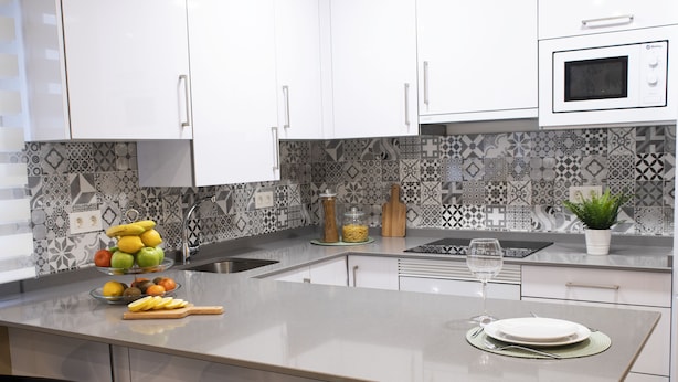 Una cocina moderna con armarios blancos, un salpicadero decorativo, una isla central con pileta y taburetes de bar.