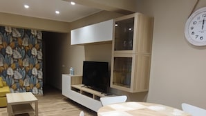 Una sala de estar moderna con una mesa de comedor de madera y sillas, un televisor de pantalla plana sobre un mueble bajo y armarios empotrados.
