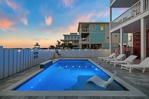 A swimming pool with lounge chairs, surrounded by a white fence, and buildings in the background. - Book for the Summer at this Gulf View, North Cape Home with Private Pool (Port St. Joe)