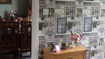 A room with a stone wall, a wooden side table with a vase of flowers, and a dining area with chairs and a chandelier.