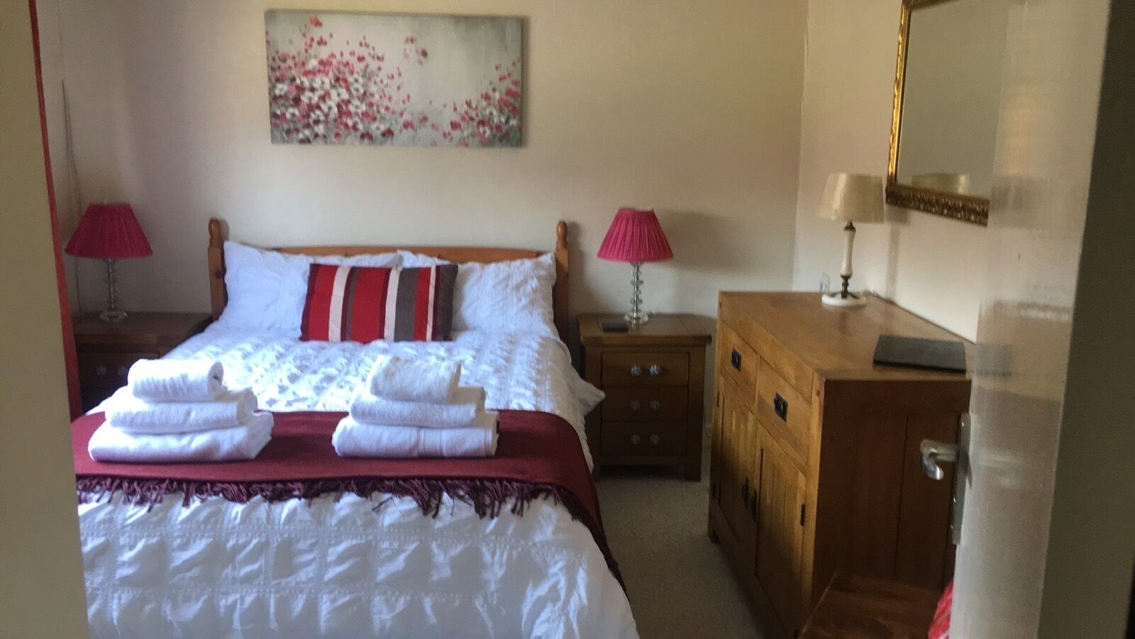 Een hotelkamer met een bed, twee nachtkastjes, een houten dressoir en een schilderij aan de muur.