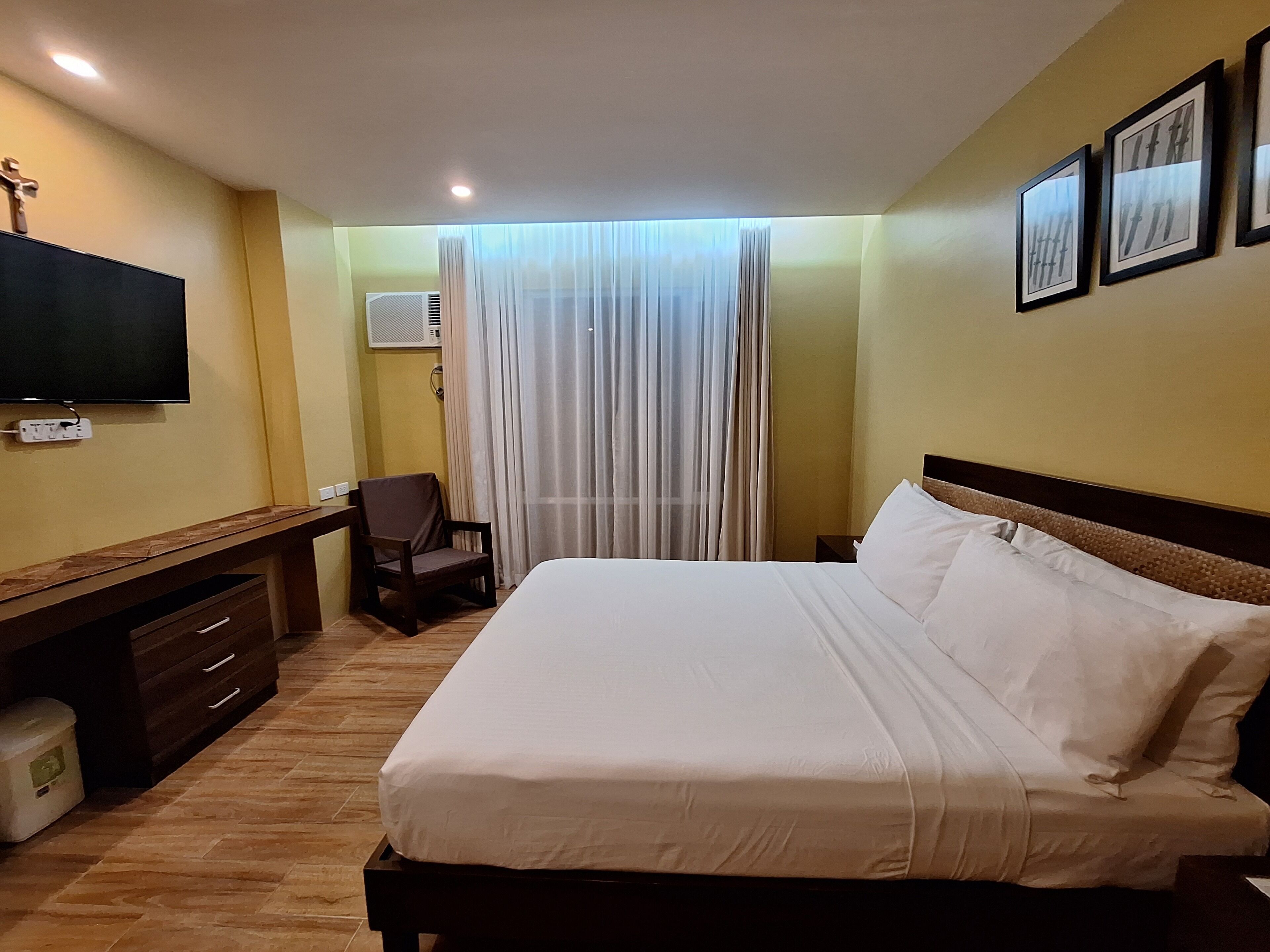 A hotel room with a bed, a desk, a chair, a TV, and a window with curtains.