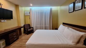 A hotel room with a bed, a desk, a chair, a TV, and a window with curtains.