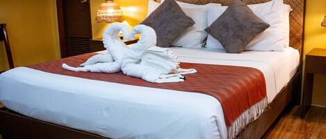 Una cama bien hecha con una manta roja, dos almohadas y un arreglo decorativo de toallas en el cabecero.