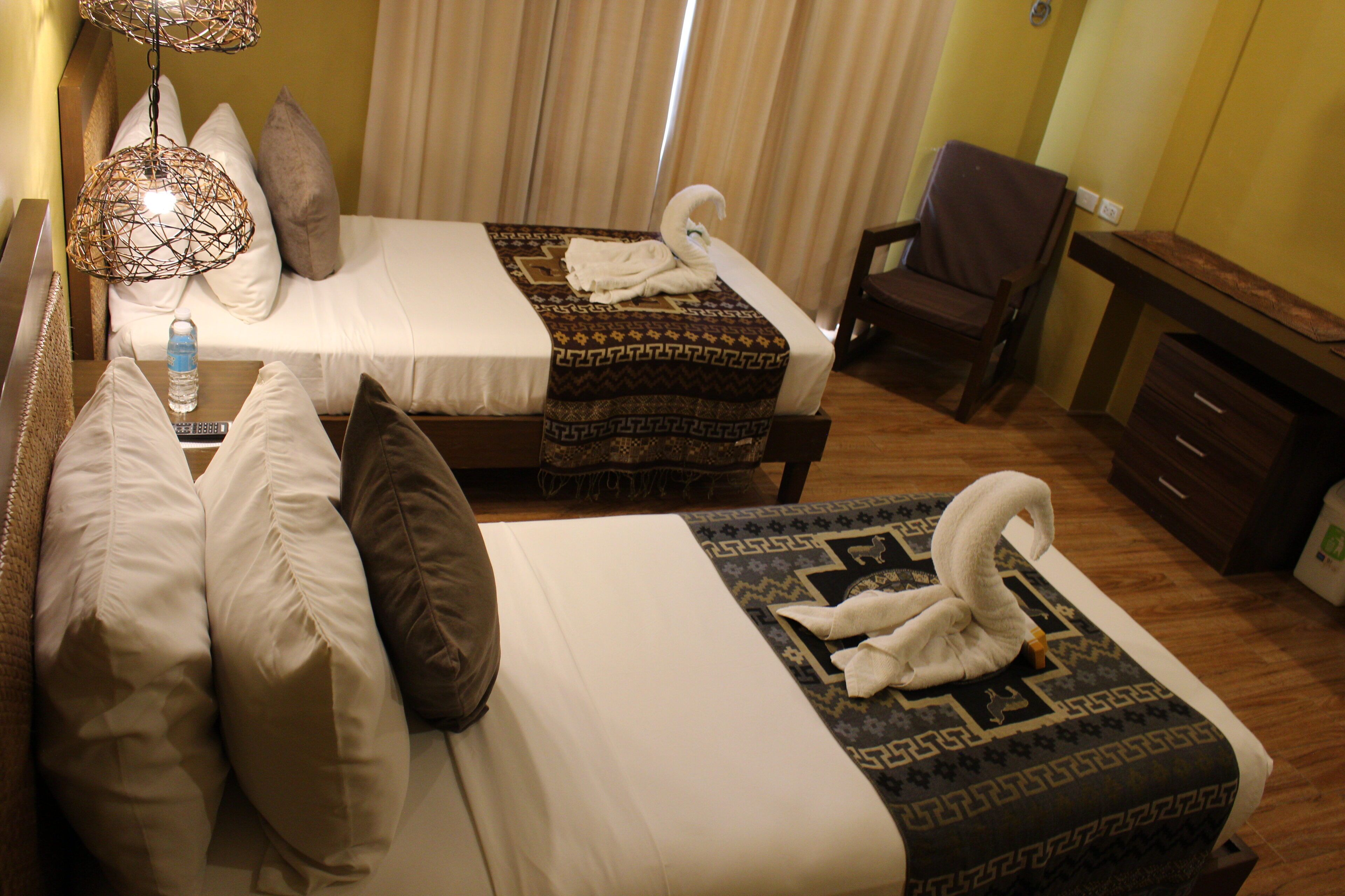 A hotel room with two beds, a desk, a chair, and a water bottle on the nightstand.