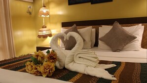 A neatly made bed with a heart-shaped towel arrangement, a decorative lamp, and a floral centerpiece.