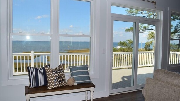 Ein Zimmer mit einer Bank an großen Fenstern mit Blick auf eine Terrasse und das Meer.