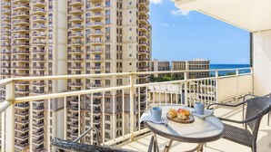 A balcony with a table, chairs, and a view of a high-rise building and the ocean.
