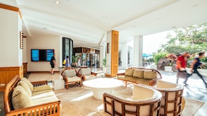 A spacious lobby with a coffee table, sofas, and chairs, a large digital display, and a view of the outside.