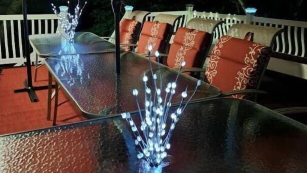 An outdoor dining area with a glass table and chairs, an umbrella, and decorative lights. - Beautiful Beach Boutique  2 Beaches, 1 lake, mature trees for beauty and privacy (Lusby)