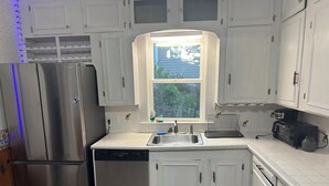 A kitchen with white cabinets, stainless steel appliances, a window, and a sink. - Biddeford Pool Beach Condo - Steps to the Sand - 1BR/1BA (Biddeford)