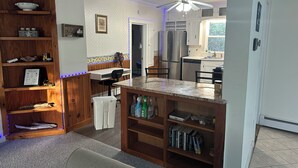 A kitchen with a wooden island, built-in shelves, a ceiling fan, and a view to the outside. - Biddeford Pool Beach Condo - Steps to the Sand - 1BR/1BA (Biddeford)