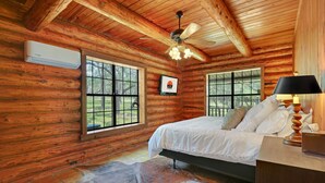 Une chambre située dans une cabane en rondins, avec un lit, un ventilateur de plafond et de grandes fenêtres.
