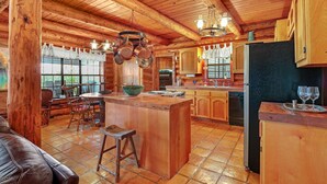 Une cabane rustique en bois dotée d’une cuisine avec un îlot central, d’un coin repas en bois et de grandes fenêtres.