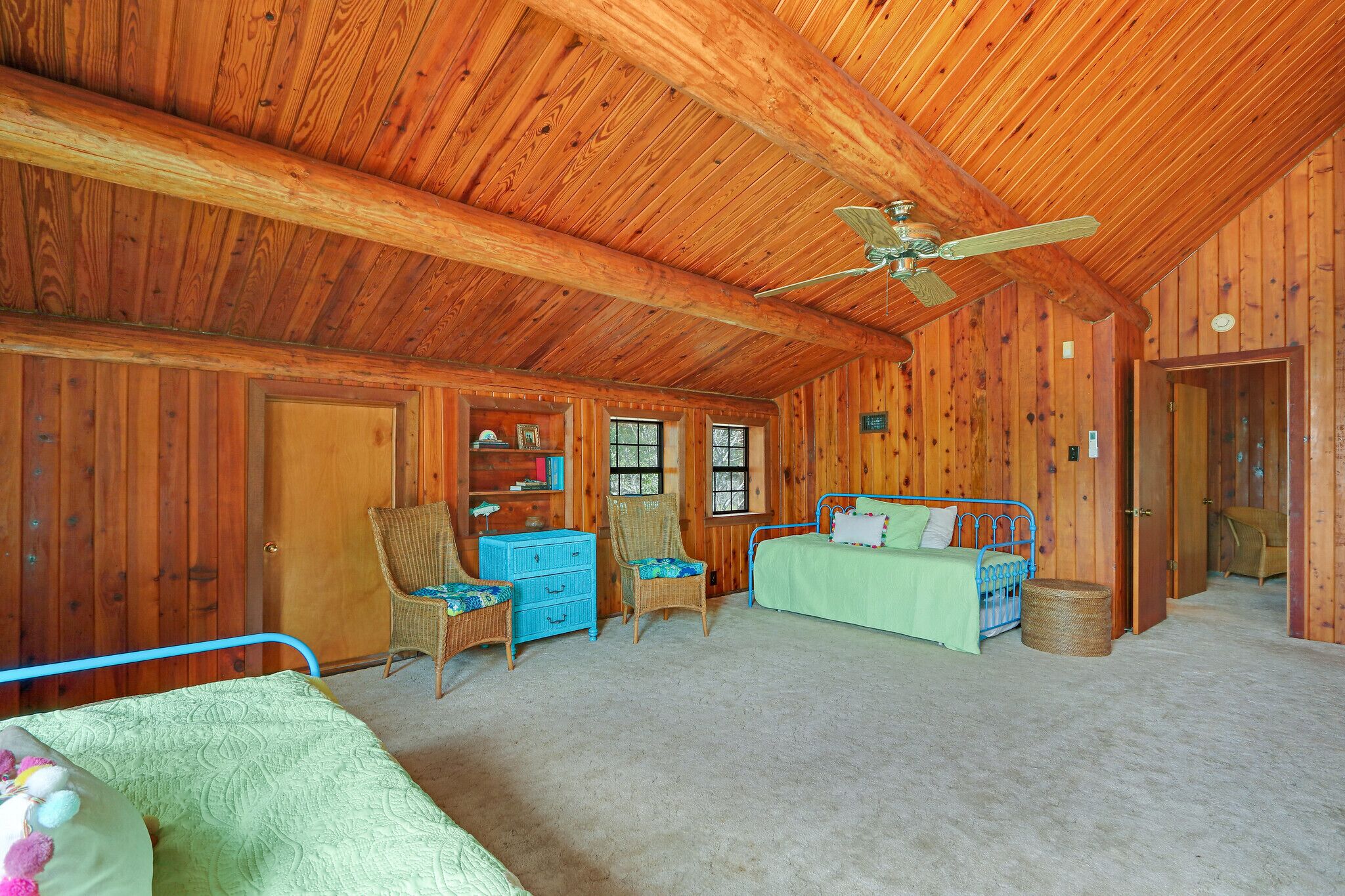 Quarto de cabana de troncos com cama, duas cadeiras, cômoda e ventilador de teto.