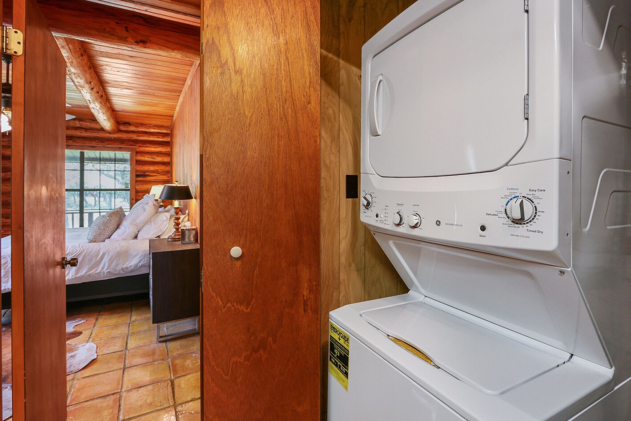 A room with a bed, a nightstand, a lamp, and a white washer-dryer unit.