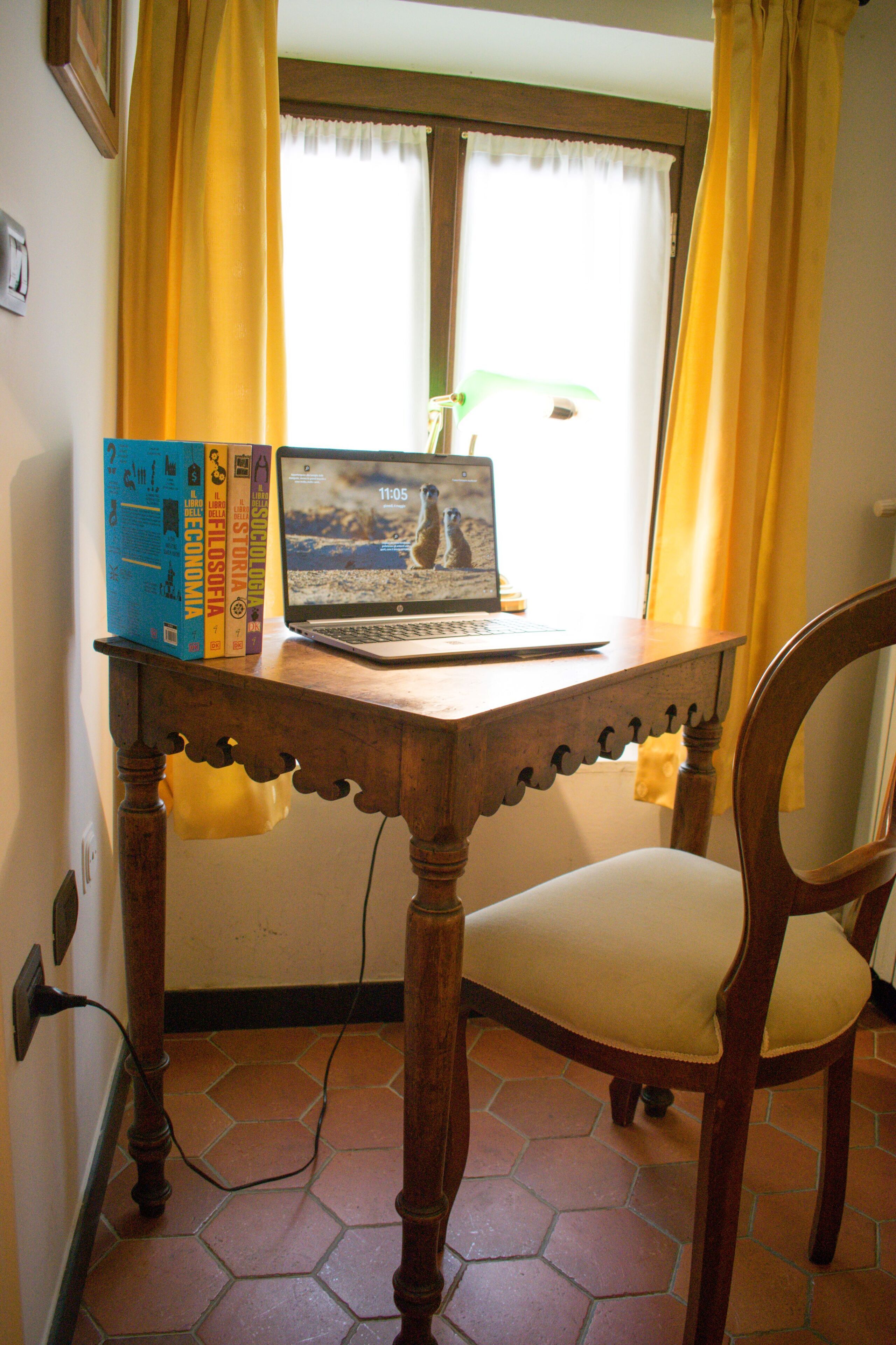 Un escritorio de madera con una computadora portátil y libros, una silla y una ventana con cortinas.