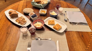 Une table ronde en bois, sur laquelle sont disposés divers aliments et boissons, notamment du pain, des pâtisseries, ainsi que des bols de fruits et des condiments.