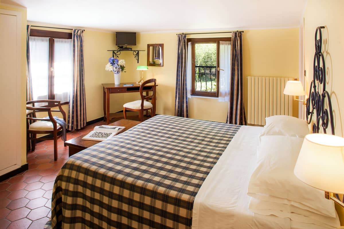 Une chambre d’hôtel avec un lit, un bureau, une chaise, une télévision et une fenêtre avec des rideaux.
