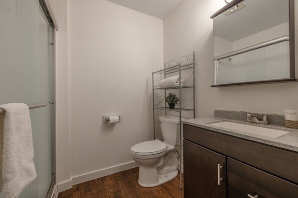A bathroom with a white toilet, a metal shelf with a towel, a mirror, and a sink with a countertop.