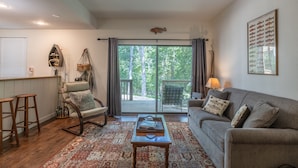 A living room with a sofa, a rocking chair, a coffee table, and a view of a deck through large windows.