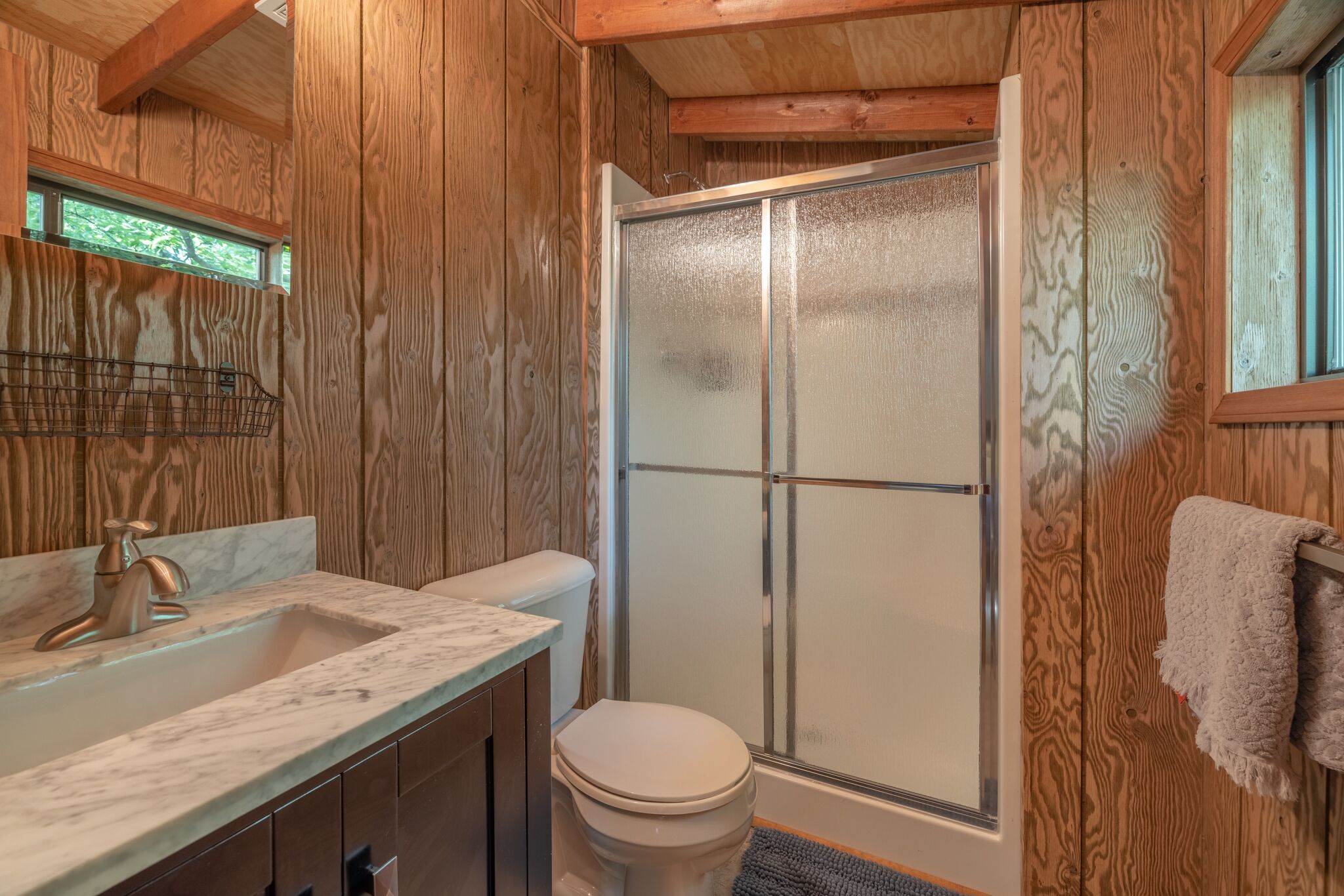 A wooden interior bathroom with a marble sink, toilet, and a glass-enclosed shower.