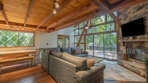 A spacious living area with a wooden ceiling, large windows, a stone fireplace, and a television mounted above it. - Reflection Point by Innsbrook Vacations! (Innsbrook)