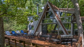 A wooden deck with outdoor furniture, a grill, and a cabin structure surrounded by trees. - Reflection Point by Innsbrook Vacations! (Innsbrook)