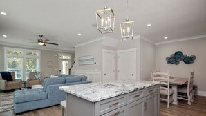 Un amplio espacio de sala con un sofá grande de color gris, una isla de cocina con armarios grises y un comedor con mesa y sillas de madera.
