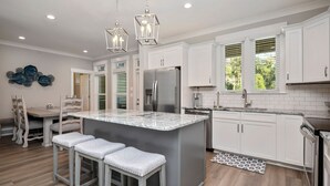 Una cocina moderna con armarios blancos, un refrigerador de acero inoxidable y una isla de mármol con taburetes de bar.