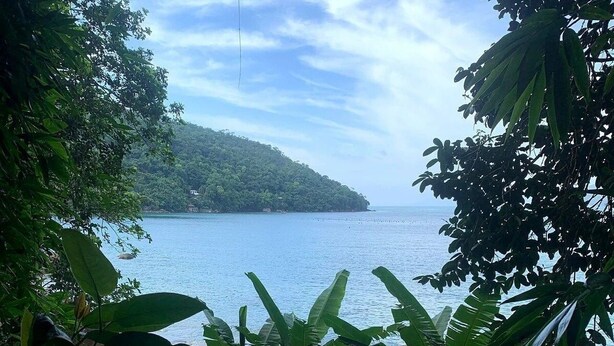 A natural landscape with a body of water, a sandy beach, and a hill in the distance. - Maranduba Ville II (Ubatuba)