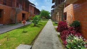 A pathway flanked by brick buildings with balconies, a grassy area, and some plants. - Maranduba Ville II (Ubatuba)