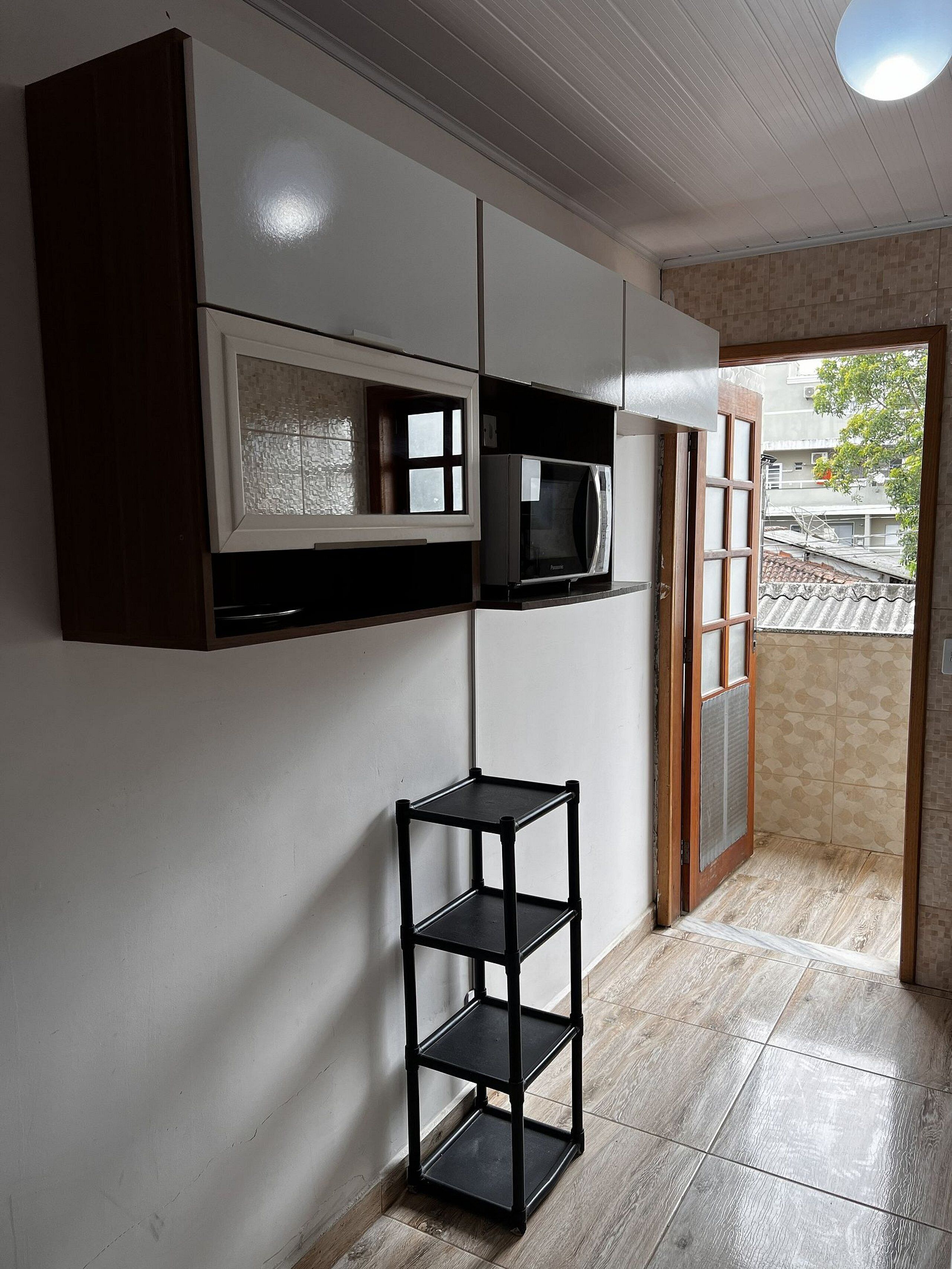 A room with a built-in microwave, a small black shelf, and a view through a door to the outside.