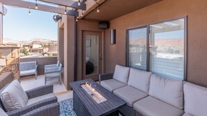 Un patio exterior con una chimenea, mobiliario de mimbre y un ventanal que da a un balcón.