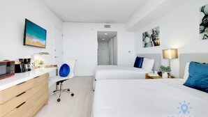 A hotel room with two beds, a desk with a microwave, a chair, and artwork on the walls. - Spectacular Studio: Balcony View, Pool, Gym (Hallandale Beach)