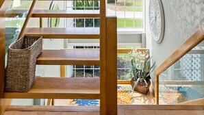Een houten trap met glazen balustrades leidt naar een balkon met uitzicht op groen.