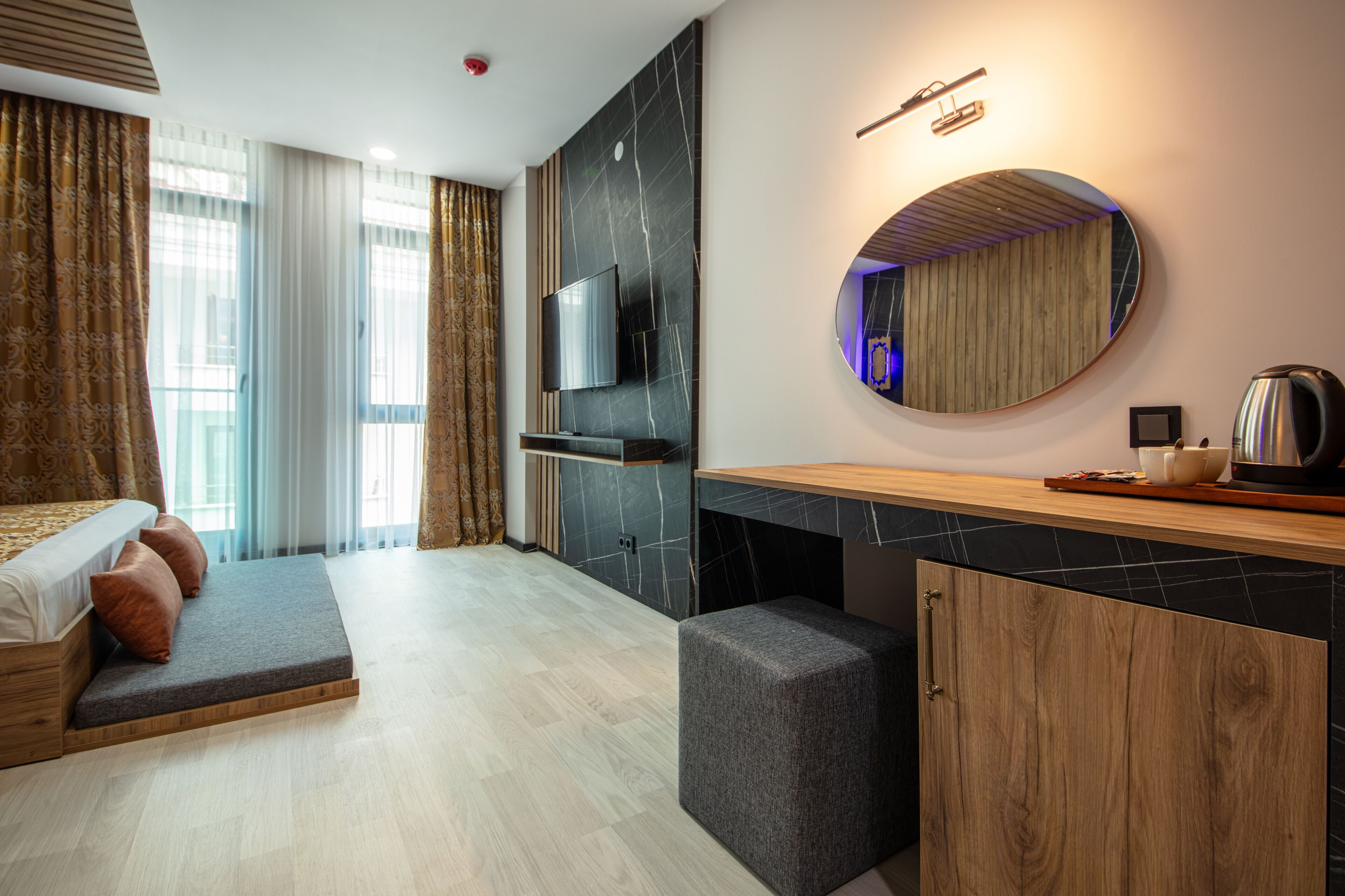A modern hotel room with a bed, a TV, a round mirror, a wooden cabinet, and a coffee maker.