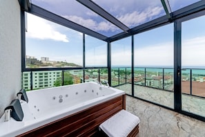 Un balcon doté d’une grande baignoire, d’un banc en bois et offrant une vue sur le paysage urbain de la côte.