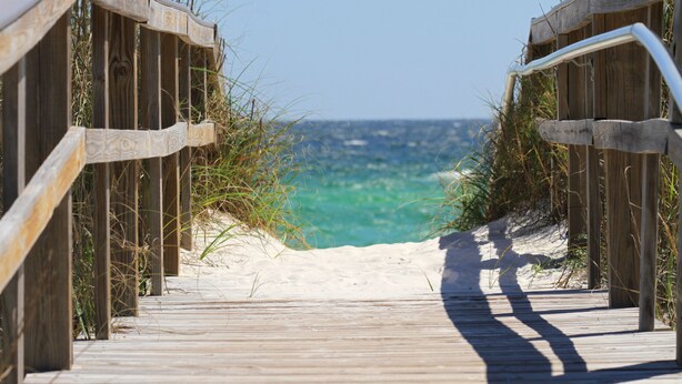 Una passerella in legno che conduce a una spiaggia sabbiosa con vista sull'oceano.