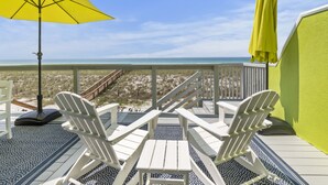 Un balcone con due poltrone Adirondack, un ombrellone giallo e vista sulla spiaggia.