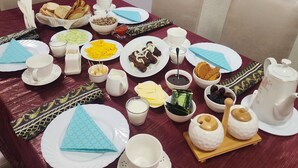 Una mesa de comedor dispuesta con varios platos, incluyendo pan, queso y embutidos, además de múltiples tazas y una tetera.