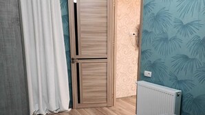 Un dormitorio con una cama, un armario de madera, un radiador y una puerta que da a otra habitación.
