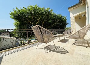 Sillas de mimbre al aire libre en un patio con baldosas, con vistas a un árbol y un edificio.