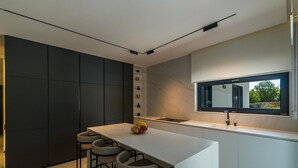 A modern kitchen with a central island, bar stools, a built-in oven, and a window above the sink. - Villa Valinka Design (Golas)