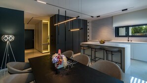 A modern kitchen with a central island, pendant lighting, and a dining area with a table and chairs. - Villa Valinka Design (Golas)