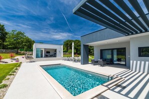 A modern house with a swimming pool, outdoor seating, and a covered patio area.