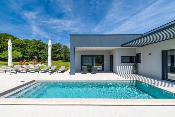 A modern house with a swimming pool, outdoor seating, and a garden.