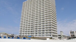 Un hotel alto de varios pisos, con numerosas balconadas, situado cerca de una playa con algunas obras en primer plano.